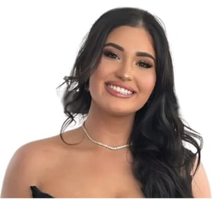 Portrait of a young woman with long black hair, hoop earrings, and a pearl necklace, smiling against a white background