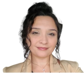 Professional headshot of a woman with dark hair in a bun, wearing a beige blazer and cross necklace against a white background